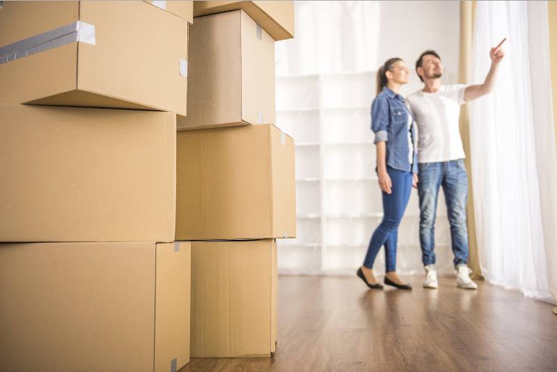 A couple standing in their new apartment with stacked moving boxes in the foreground, symbolizing a successful and organized moving process.