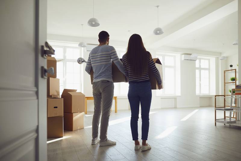 A couple carrying moving boxes into a bright high-rise apartment – SB Movers High-Rise Building Moving services ensure a smooth and efficient relocation.