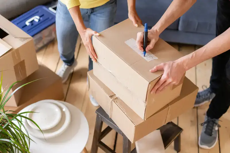 A couple labeling moving boxes during a home relocation – SB Movers House Moving services provide efficient and stress-free moving solutions.