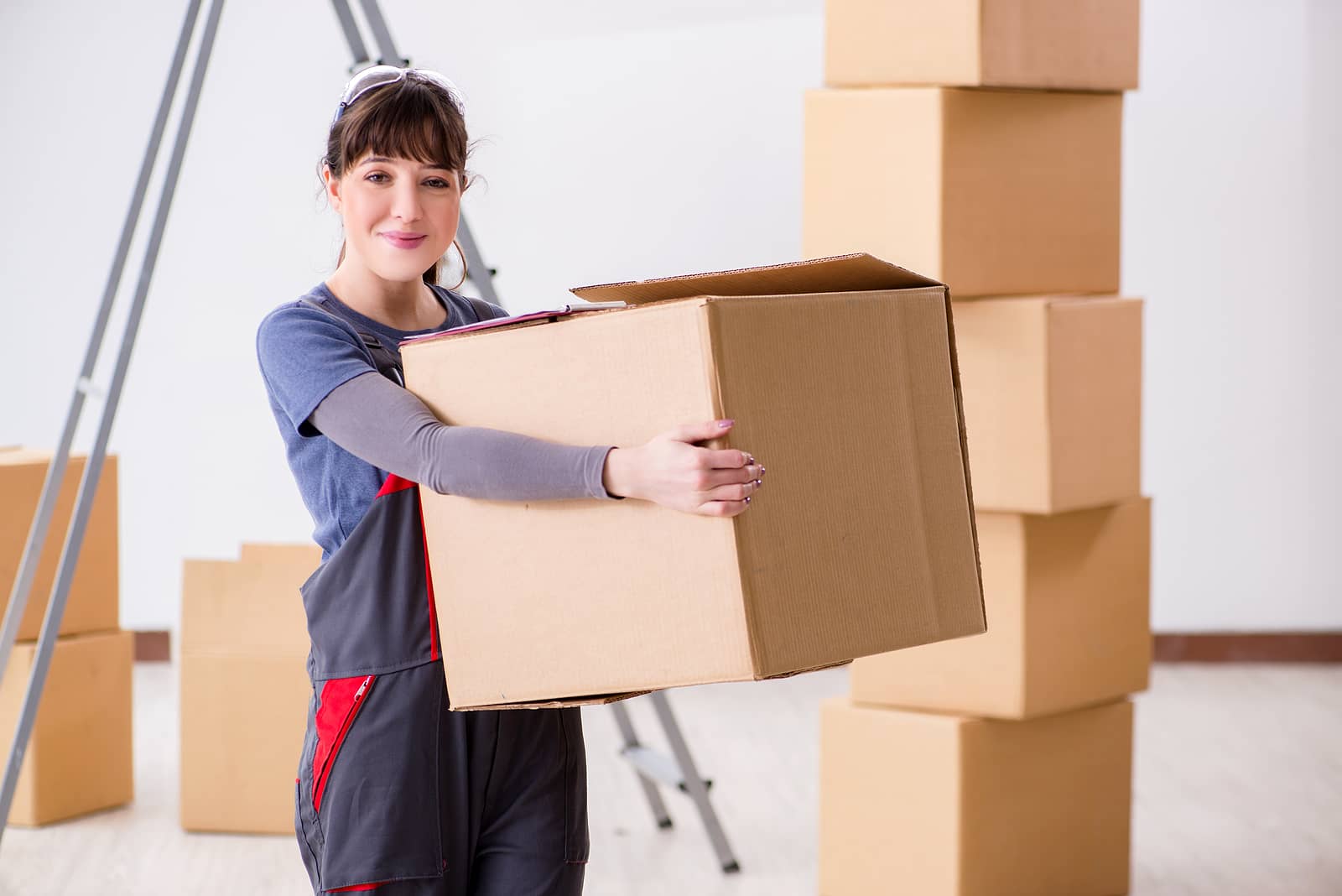 A professional mover carrying a box with stacked moving boxes in the background – SB Movers Townhouse Moving services ensure a smooth and efficient relocation.