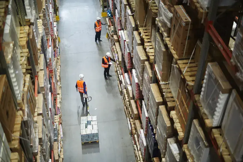 Warehouse workers in safety vests managing inventory and moving goods in a large industrial storage facility Vaughan Movers By SB Movers